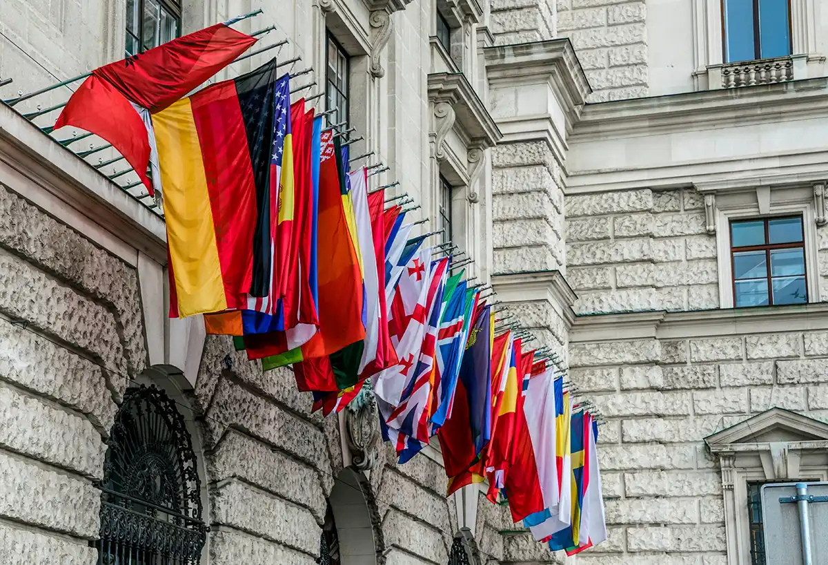 Hilera de banderas nacionales en la fachada de un edificio diplomático, símbolo de las representaciones internacionales que mantiene un servicio exterior en todo el mundo.