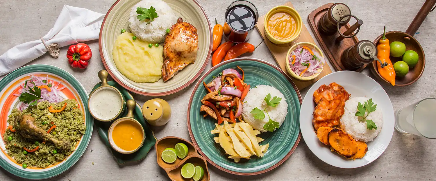 Vista cenital de platos peruanos: arroz con pato, lomo saltado con papas fritas, pescado a la plancha, salsas de ají amarillo, ensalada de cebolla morada y limones.